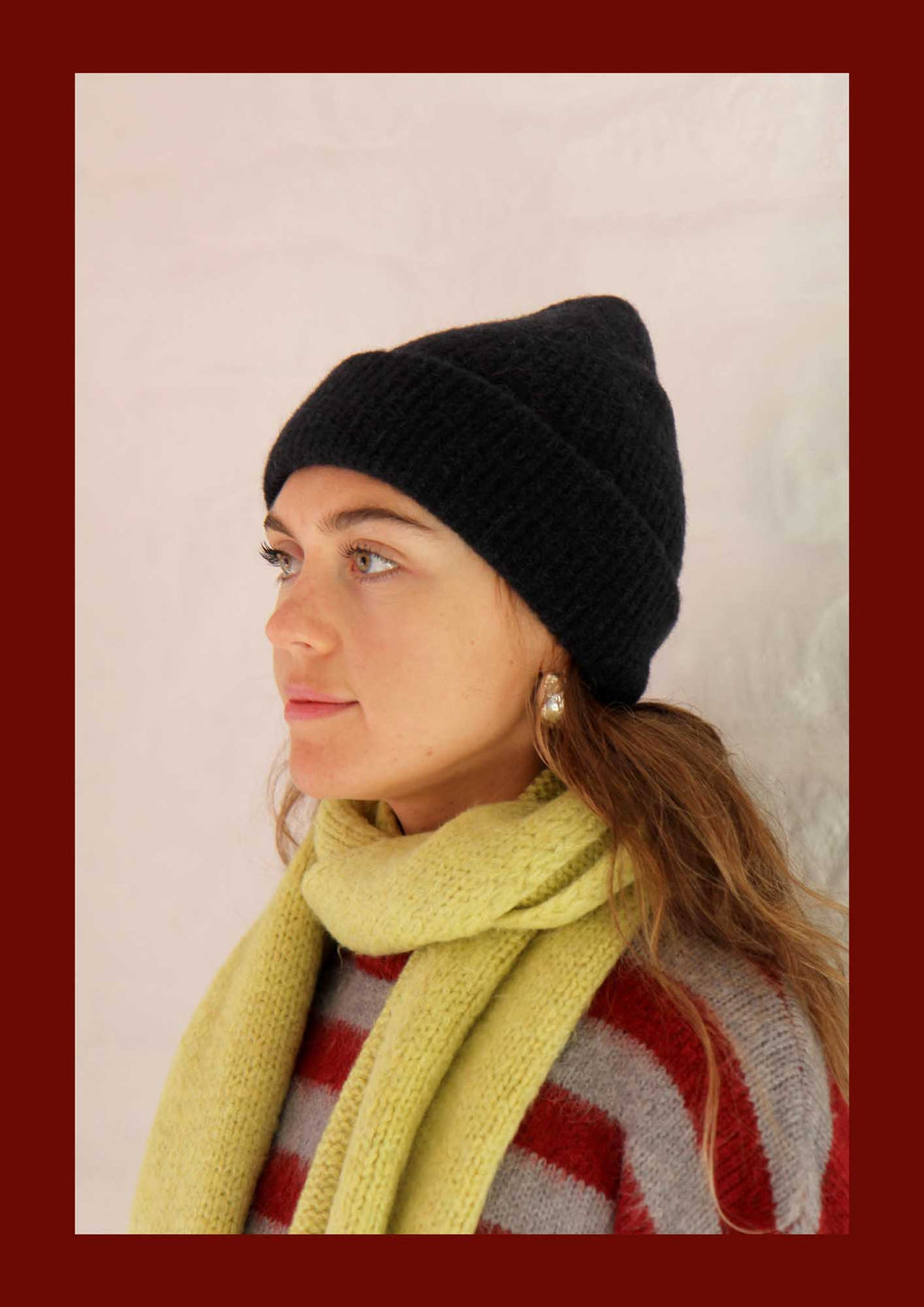 Woman wearing a black beanie and yellow scarf against a plain background