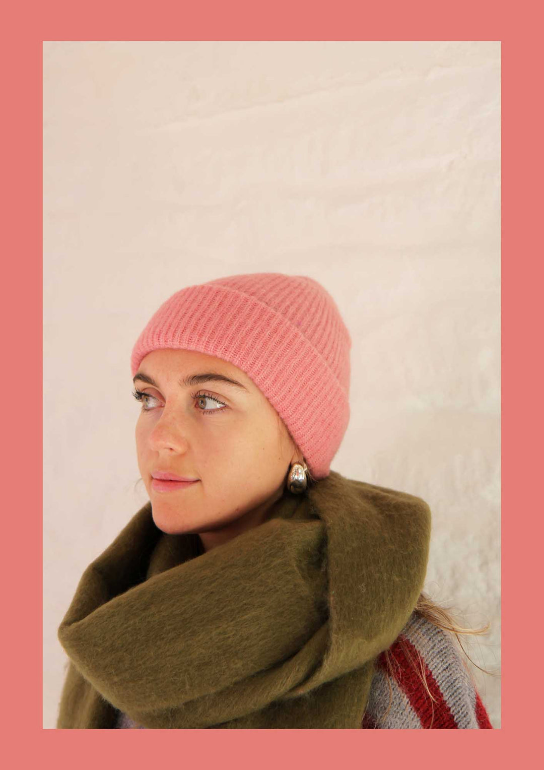 Woman wearing a pink knitted beanie and green scarf against a light background