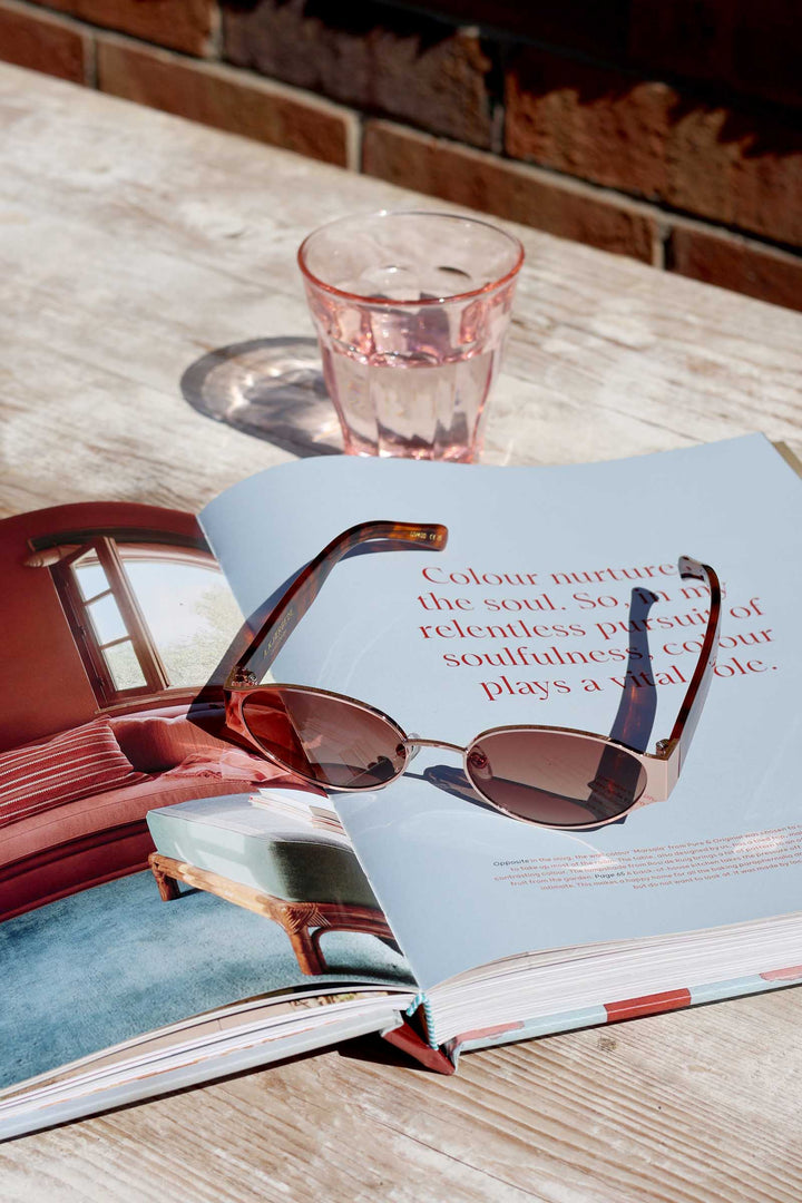 Sunglasses on an open book with a glass of water on a wooden table.