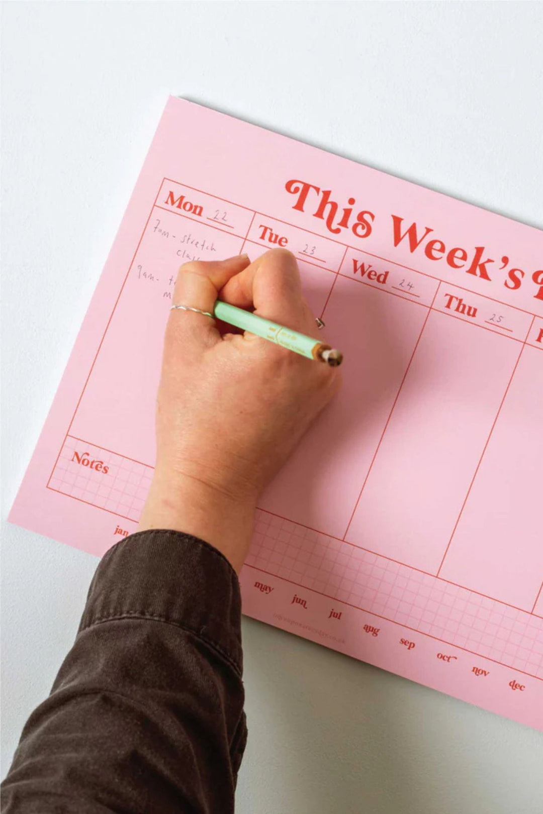 Hand writing on a pink weekly planner with a pen.