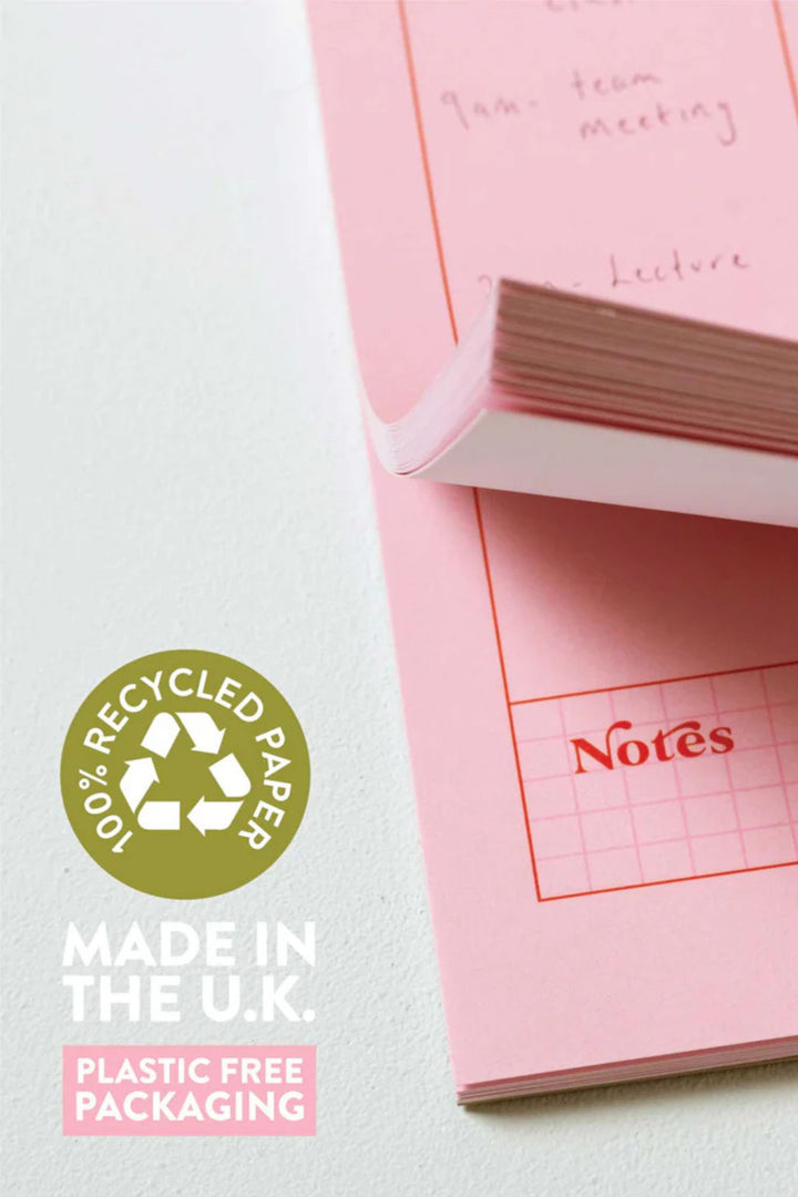 Pink notepad with grid lines and 'Notes' text, featuring a recycling logo and text about recycled paper and plastic-free packaging.