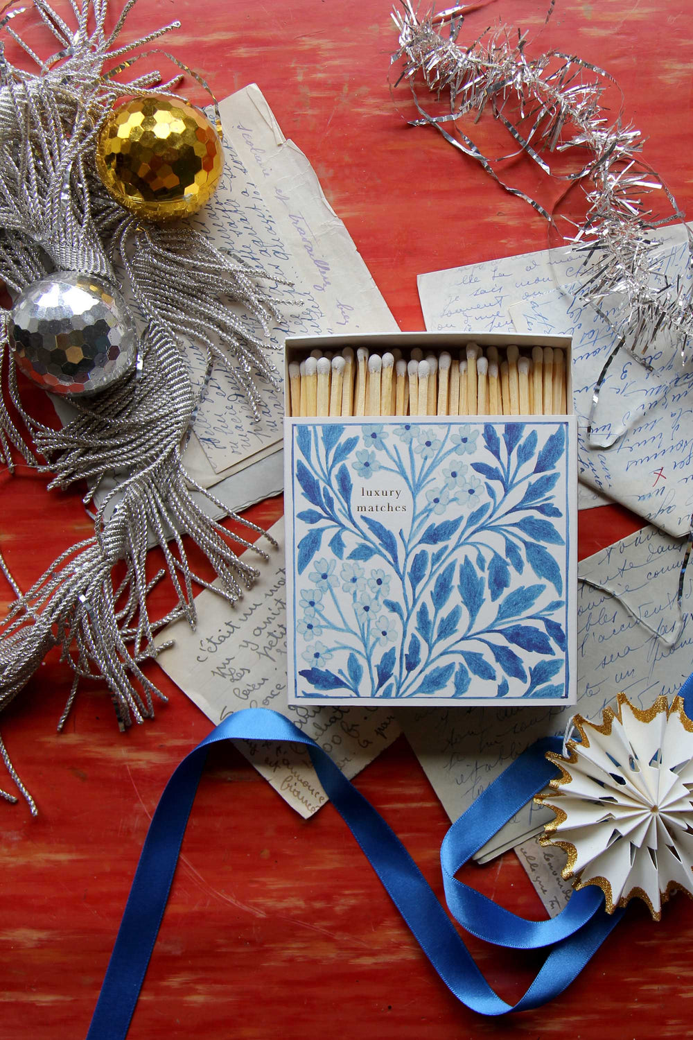 Decorative matchbox with floral design on a festive background with tinsels and ribbons.