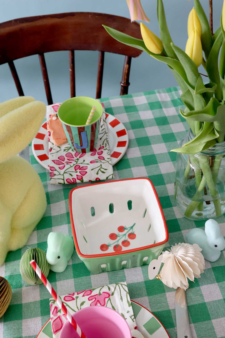 Children's table setting with colorful plates, cups, and toys on a green checkered tablecloth.