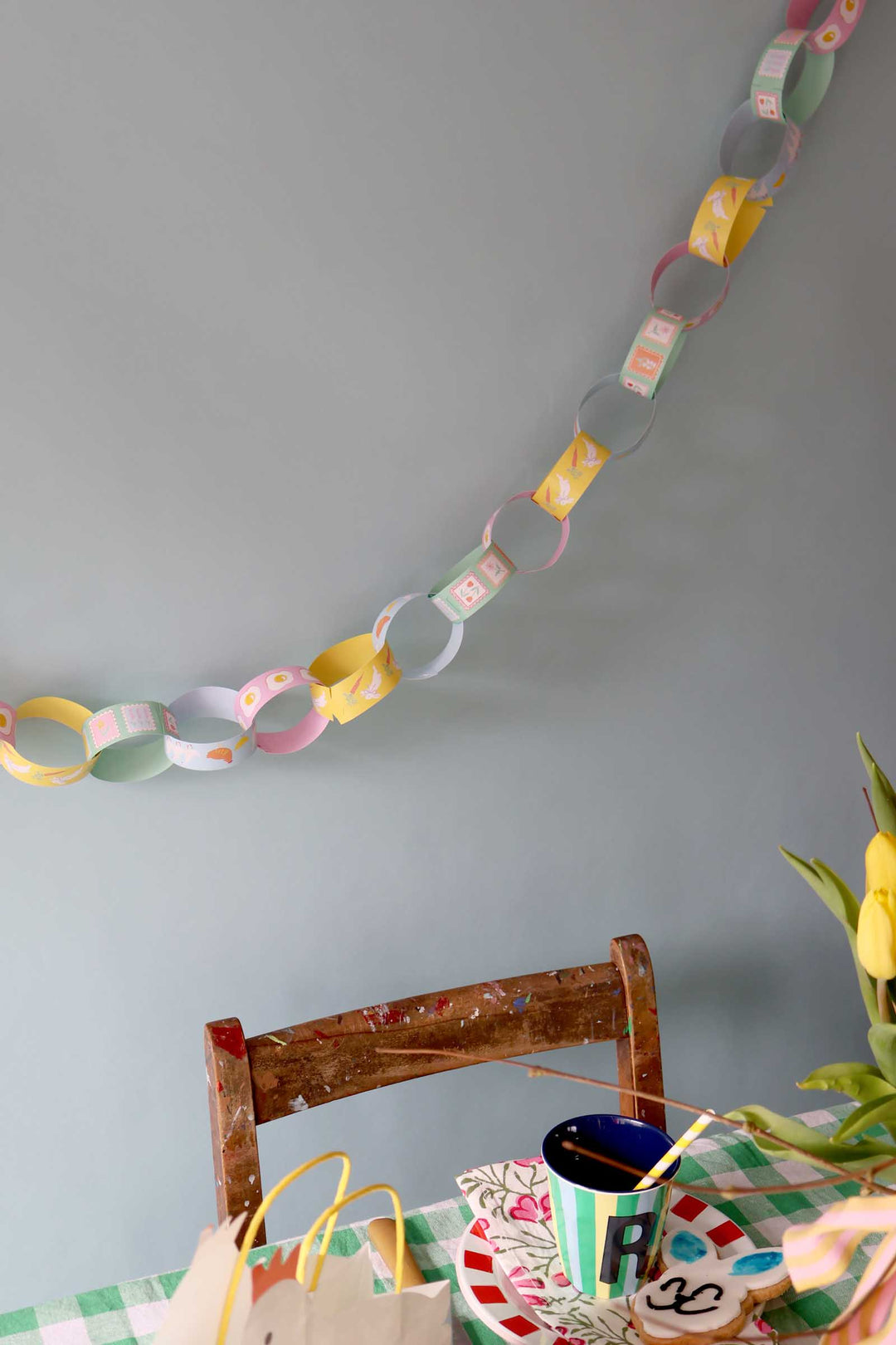 Colorful paper chain hanging on a gray wall above a table with a cup, cookies, and a plant.
