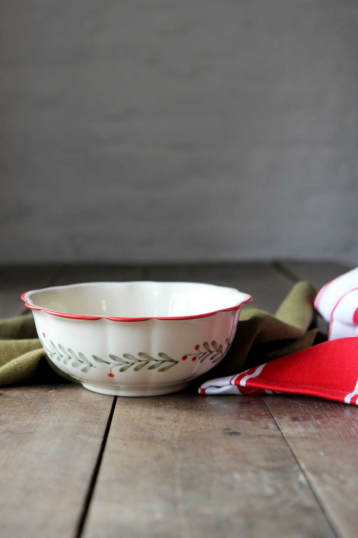 White ceramic bowl with red rim and floral patterns on a wooden surface with green and red napkins.