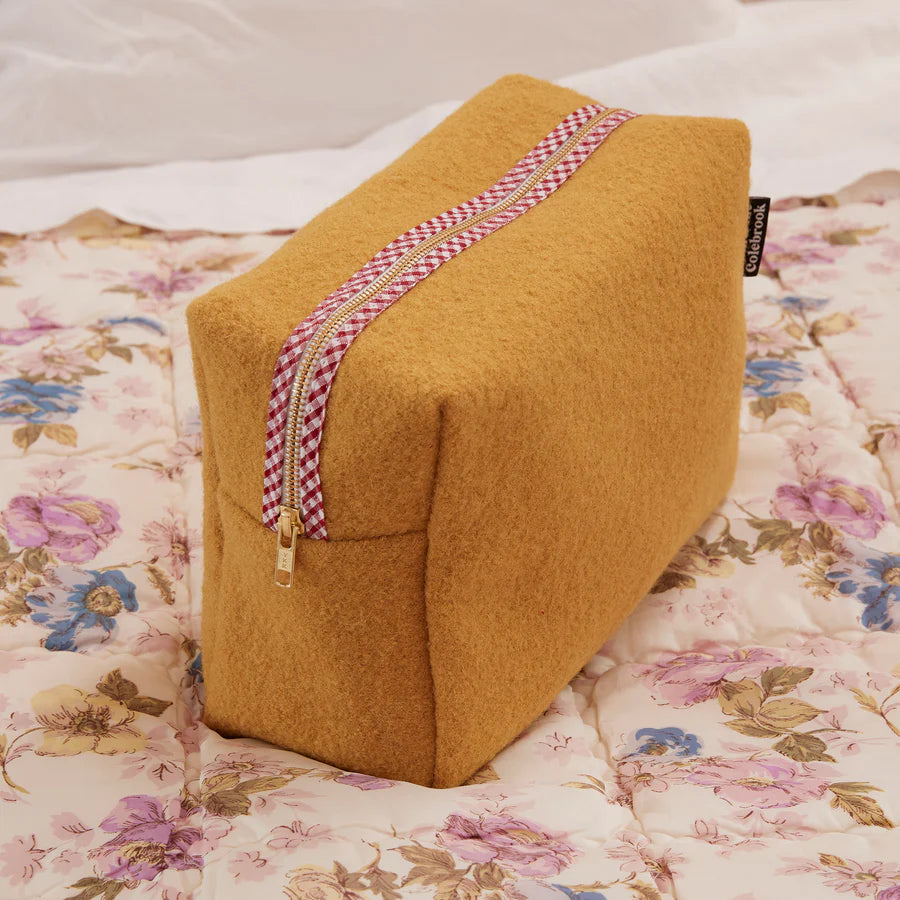 Brown wedge-shaped pillow with a zipper on a floral bedspread