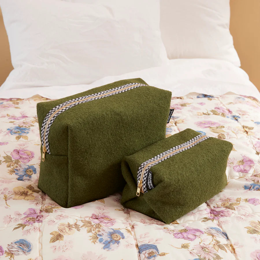 Two green wedge pillows with decorative straps on a floral bedspread.