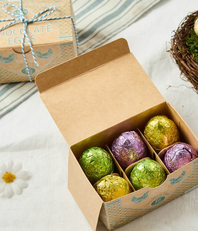 Box of colorful Easter eggs with a decorative gift box in the background.