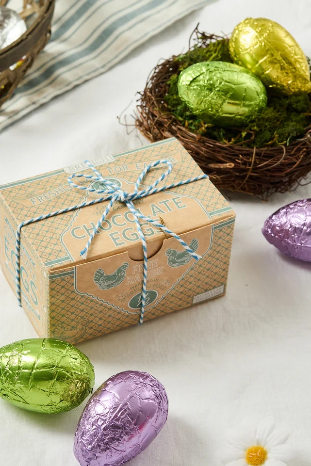Box of chocolate eggs with green and purple foil-wrapped eggs on a white surface.