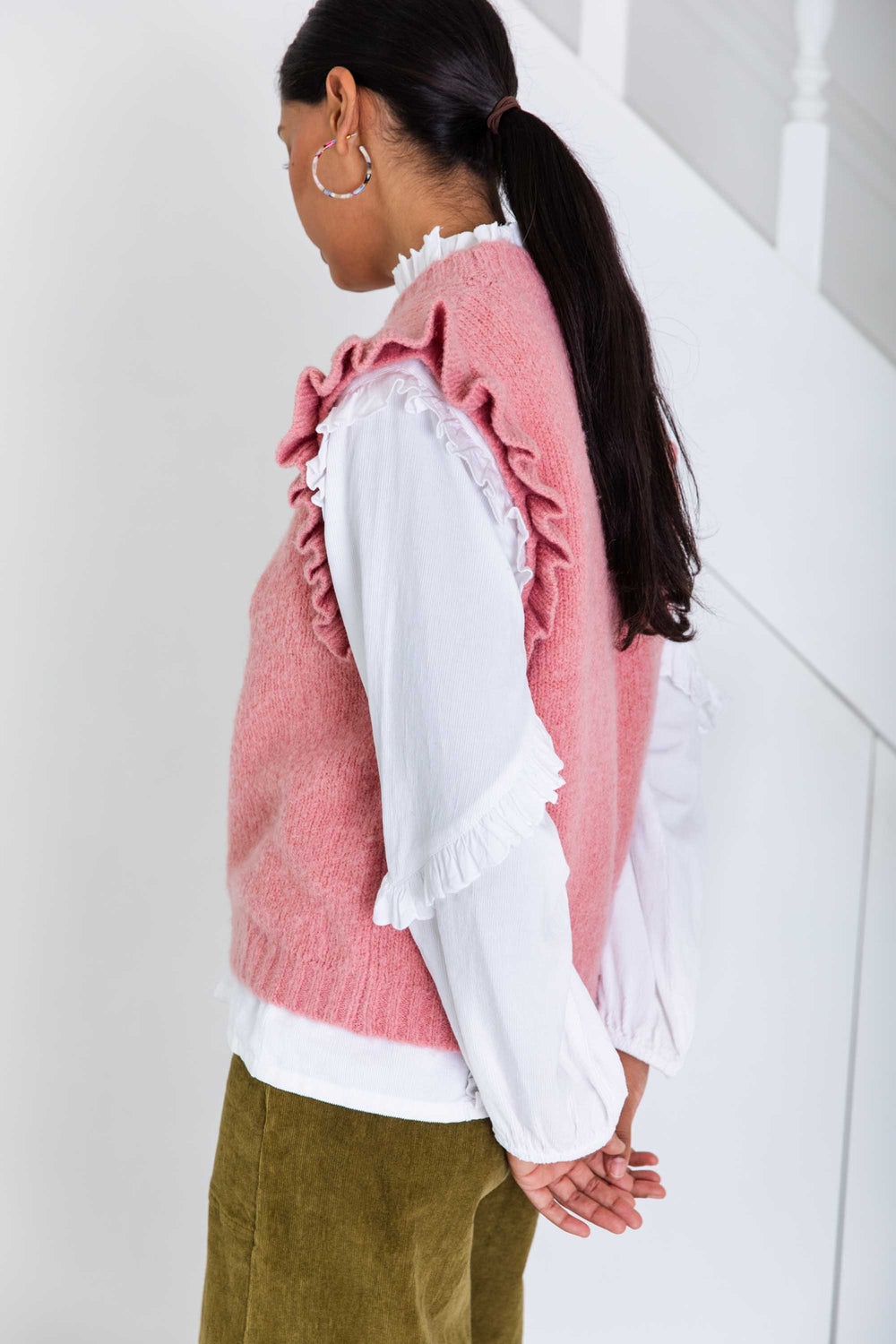Person wearing a pink ruffled vest over a white shirt with a white background