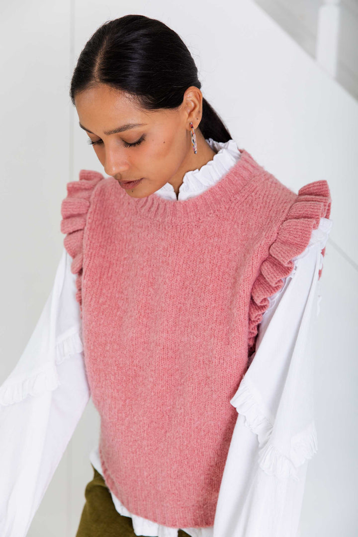 Woman wearing a pink knitted vest with ruffled sleeves against a white background