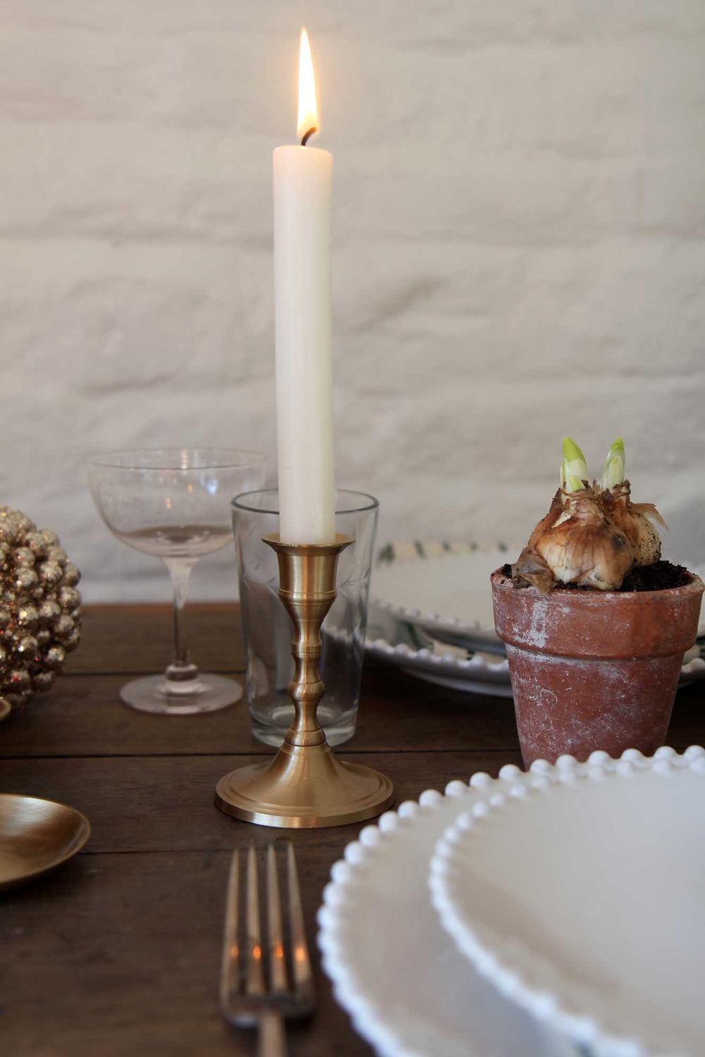 Candlelit table setting with a potted plant, glasses, and cutlery on a wooden surface.