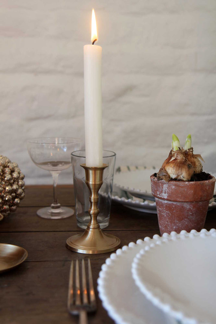 Candlelit table setting with a potted plant, glasses, and cutlery on a wooden surface.