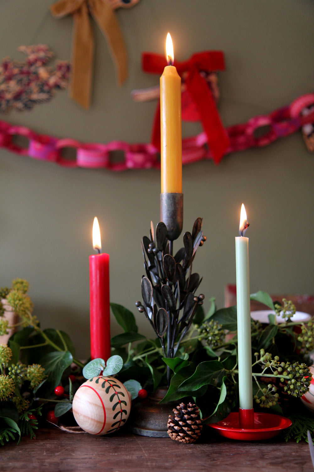 Decorative setup with candles, greenery, against a wall with festive decorations.
