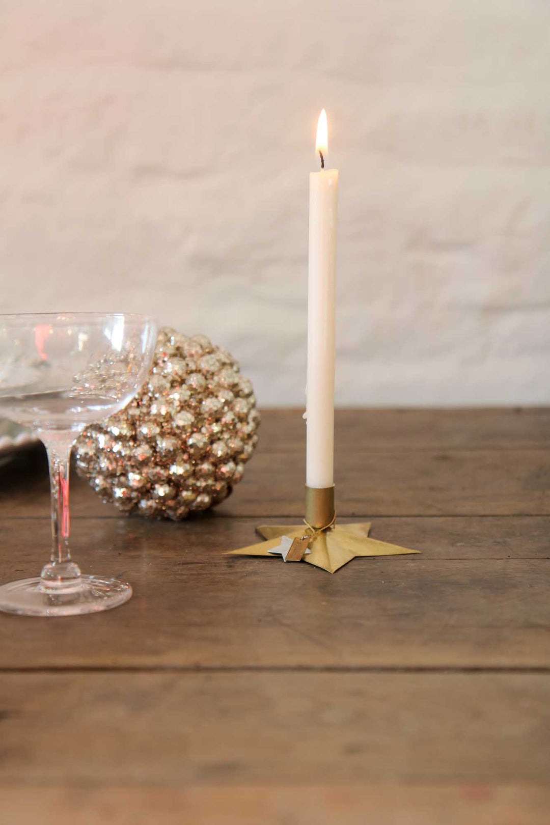 Candle on a gold holder with a textured ball and glass object on a wooden surface.
