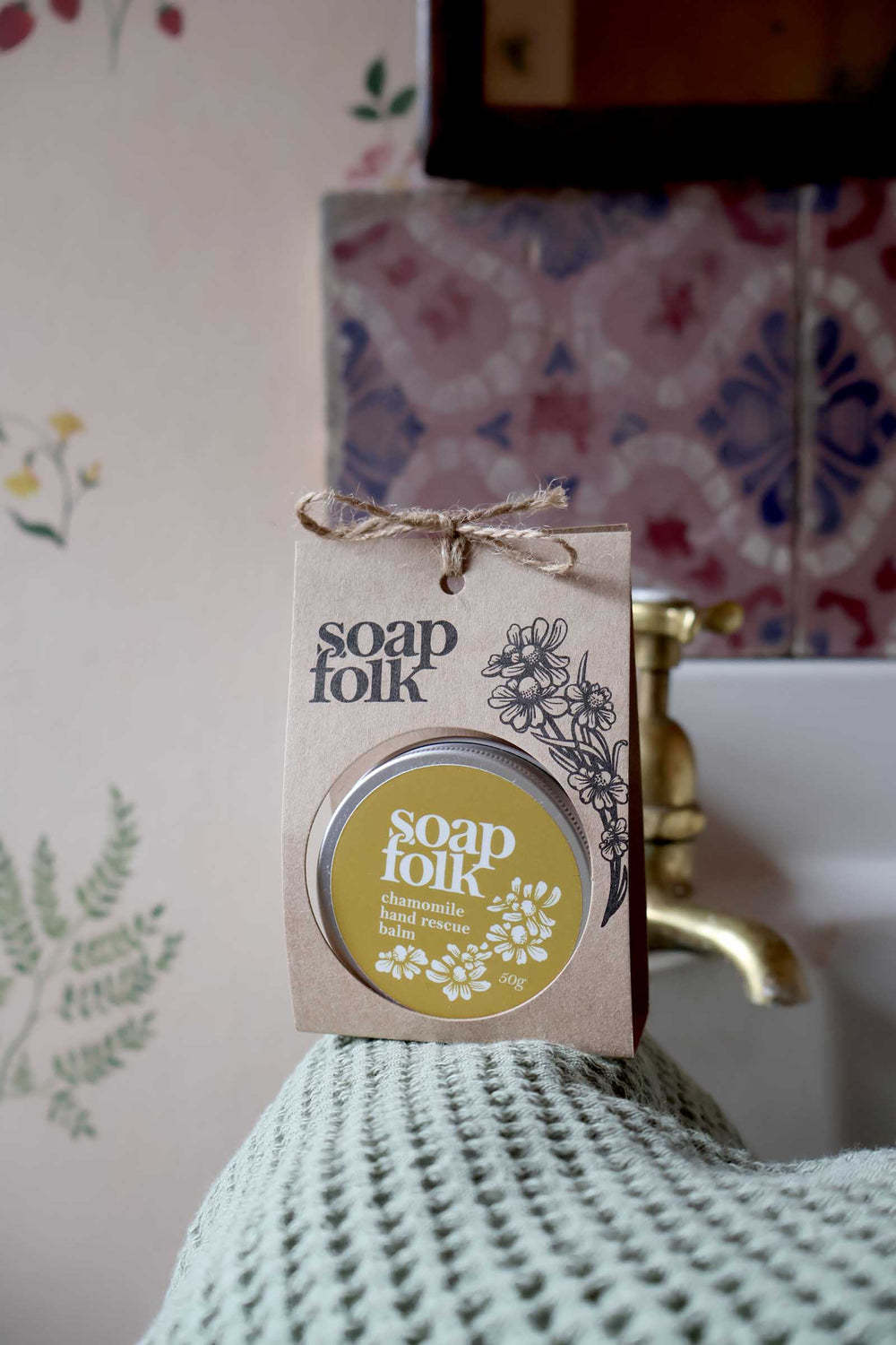 Soap Folk product packaging on a textured surface with a floral-patterned wall in the background