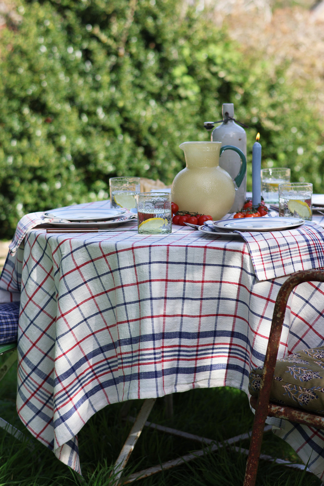 Outdoor table setting with a plaid tablecloth, glasses, plates, and a pitcher.