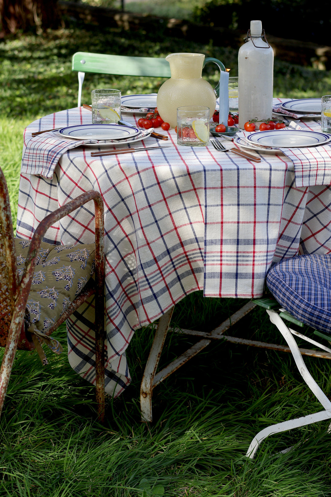 Outdoor table setting with plaid tablecloth, chairs, and picnic items on grass