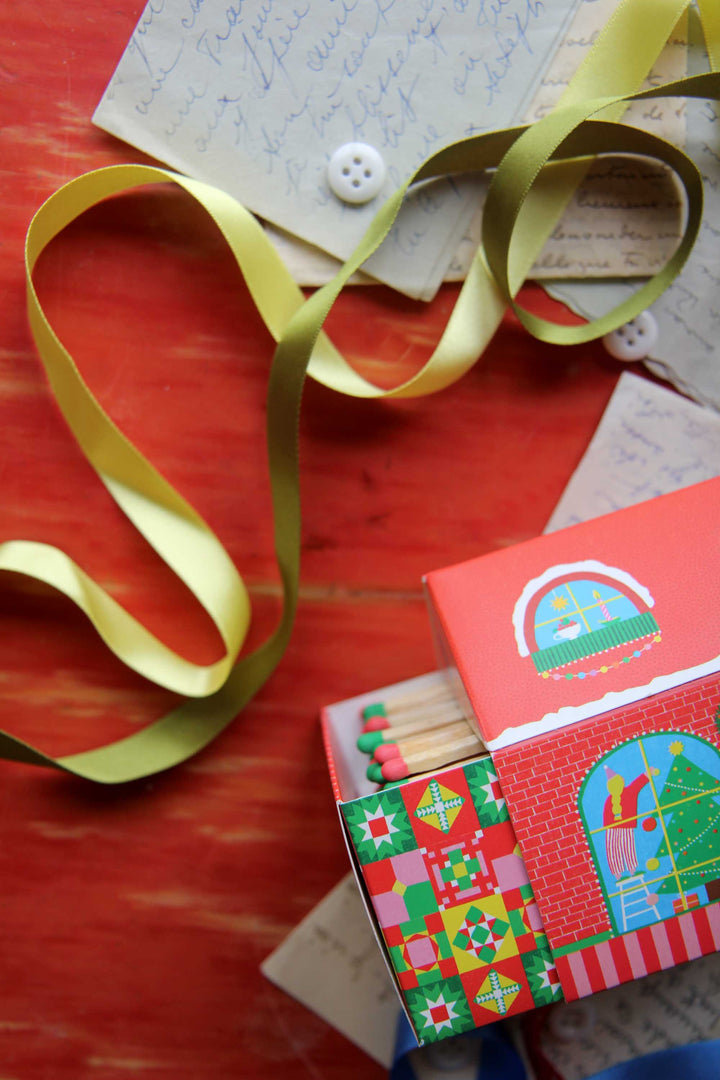 Matches in a decorative match box with a green ribbon on a red surface