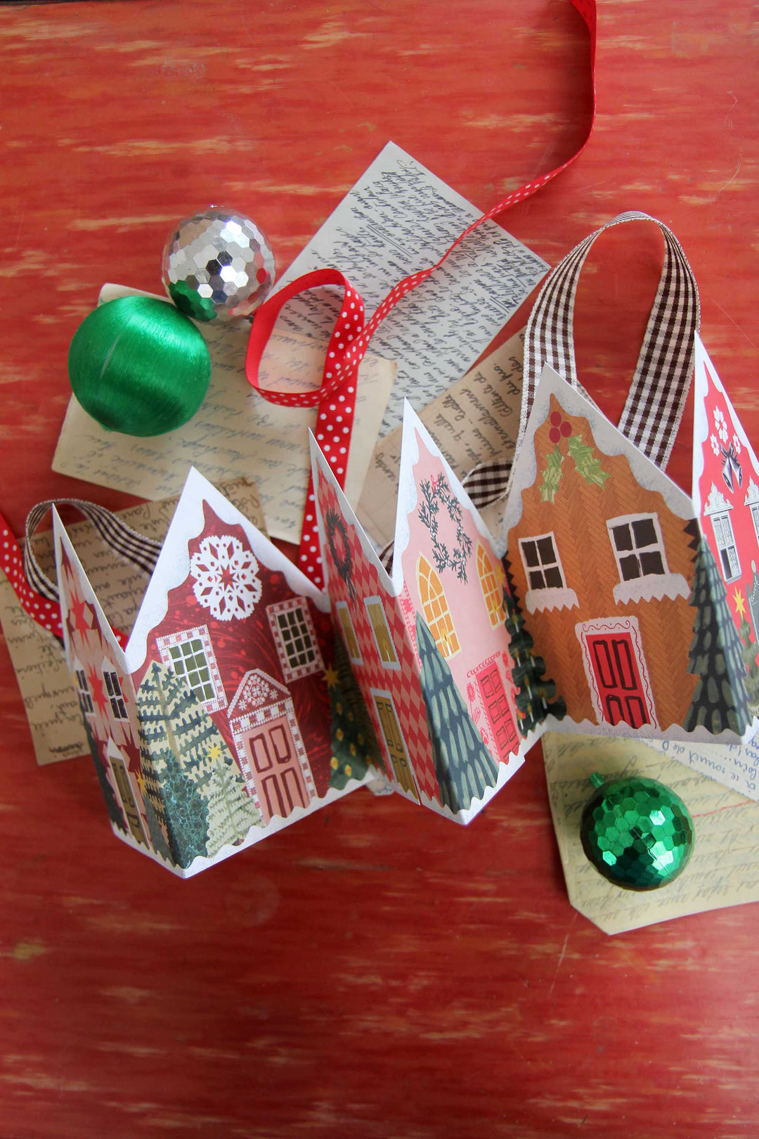 Decorative paper houses with green ornaments on a wooden surface