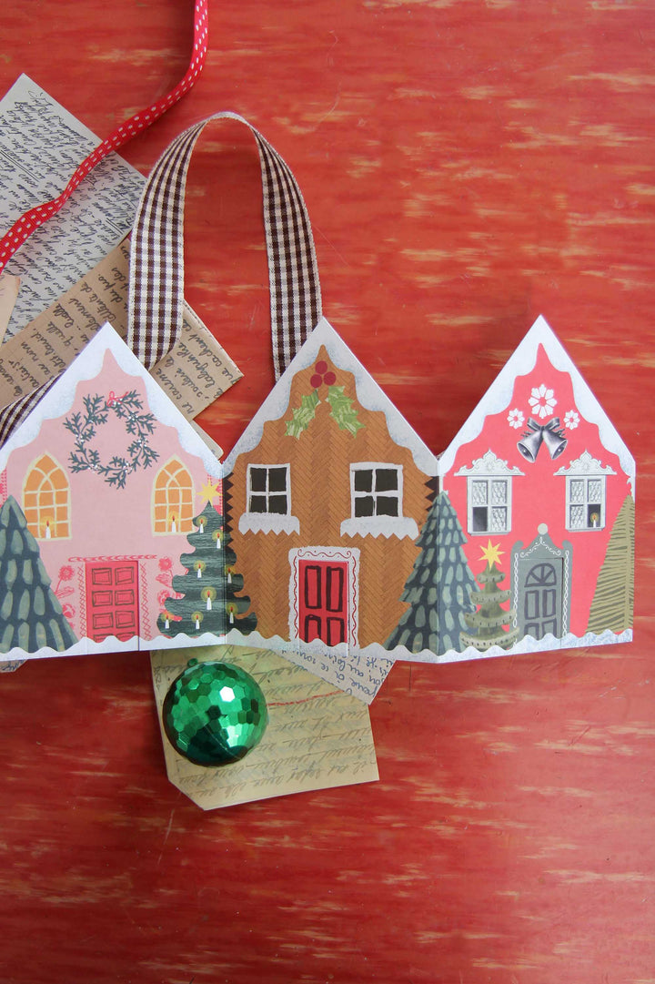 Decorative paper houses with a green ball on a red wooden surface
