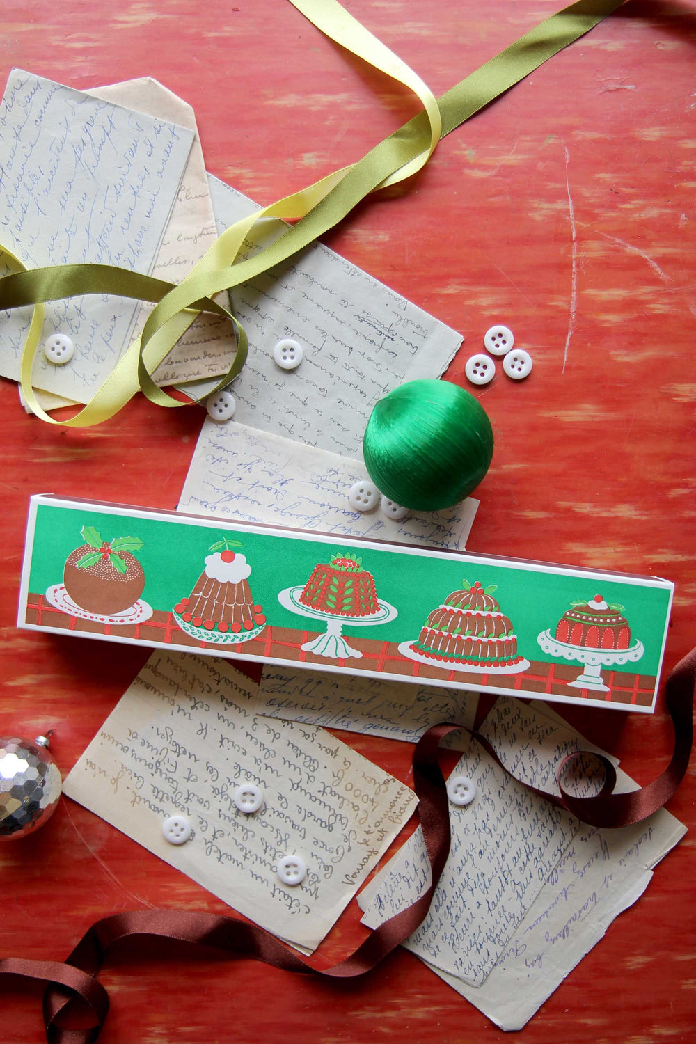 Decorative matches with cake illustrations on a red surface with ribbons and buttons.