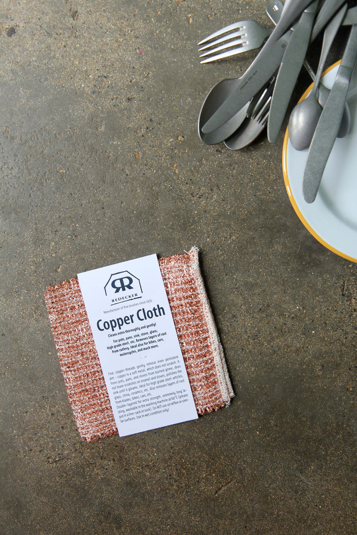 Copper cloth with a label on a concrete surface next to cutlery.