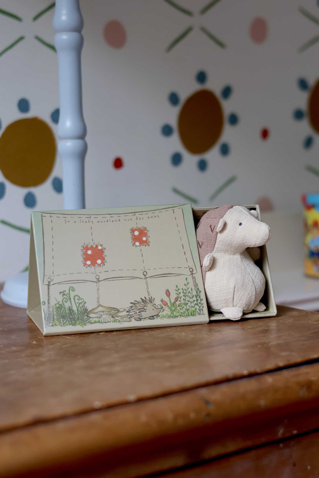 Small card with a design and a plush toy on a wooden surface with a colorful polka dot wall in the background.
