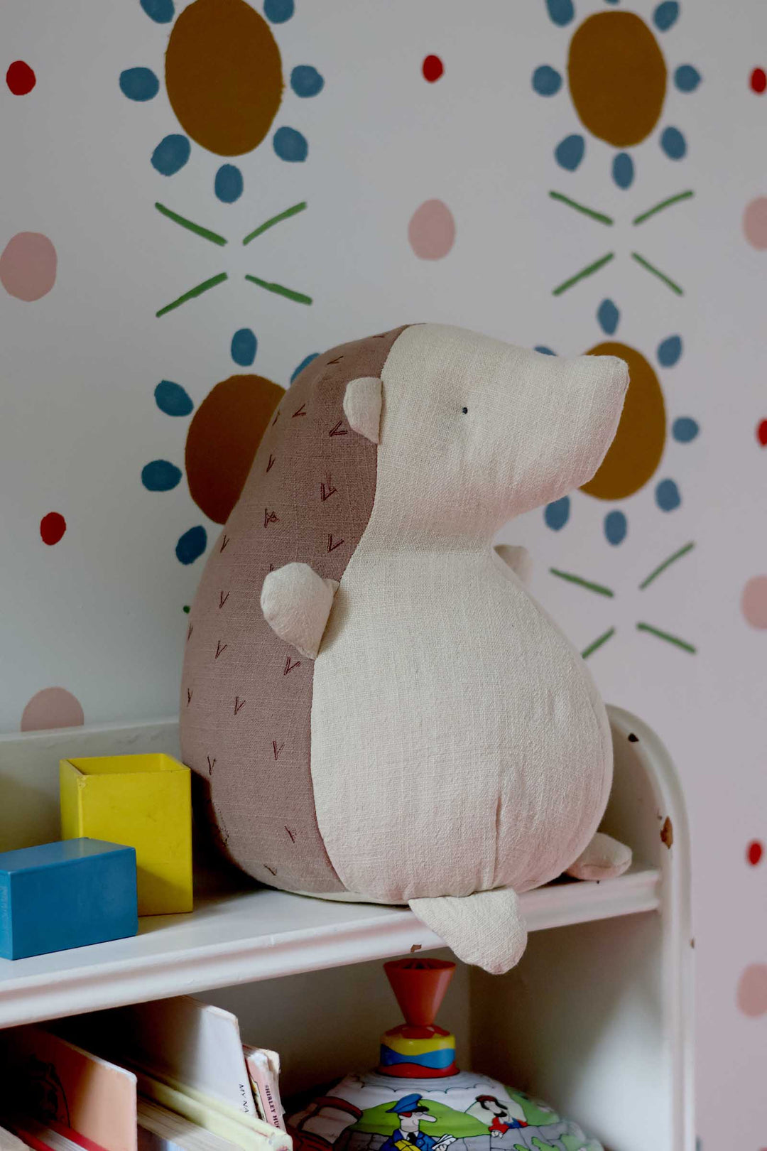 Plush toy hedgehog on a shelf with colorful wall design in the background