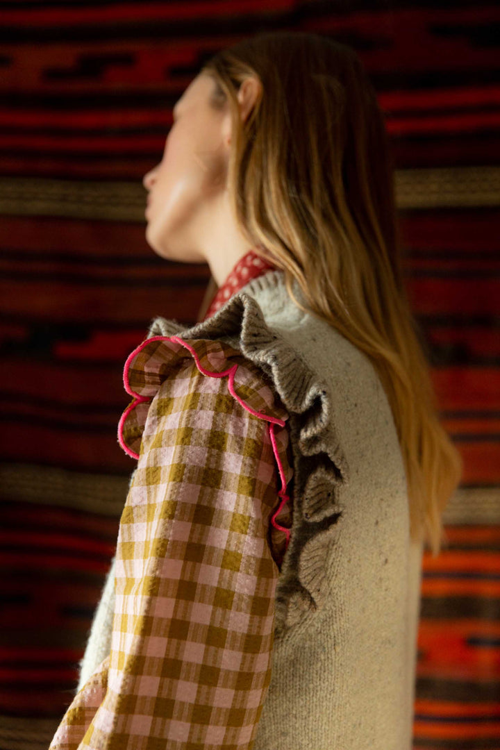 Person wearing a checkered dress with ruffled details against a textured red wall.