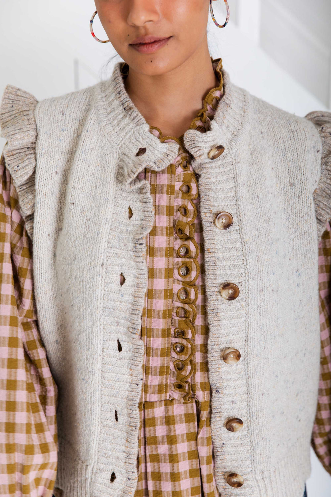Person wearing a textured vest over a plaid shirt with a neutral background