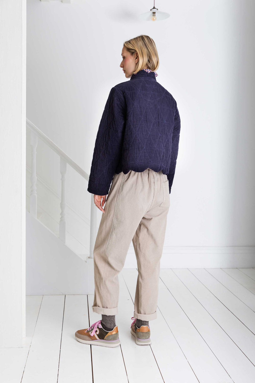 Person wearing a dark blue jacket and beige pants in a minimal white room.