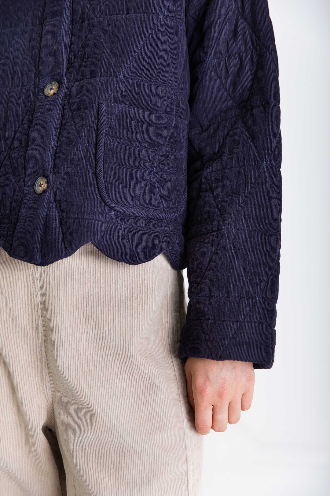Person wearing a dark blue quilted jacket and beige pants on a white background