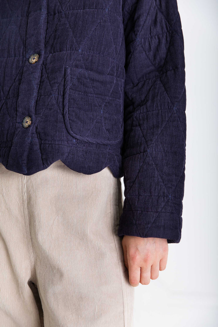 Person wearing a dark blue quilted jacket and beige pants on a white background