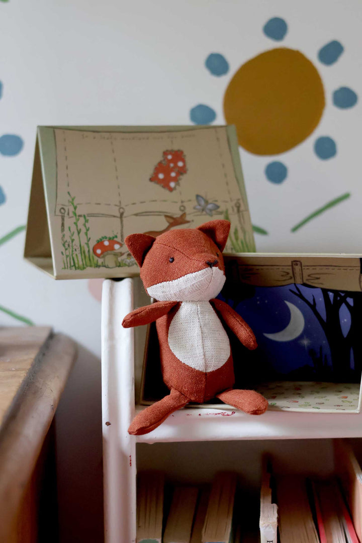 Plush fox toy on a shelf with a children's book and colorful wall design in the background.