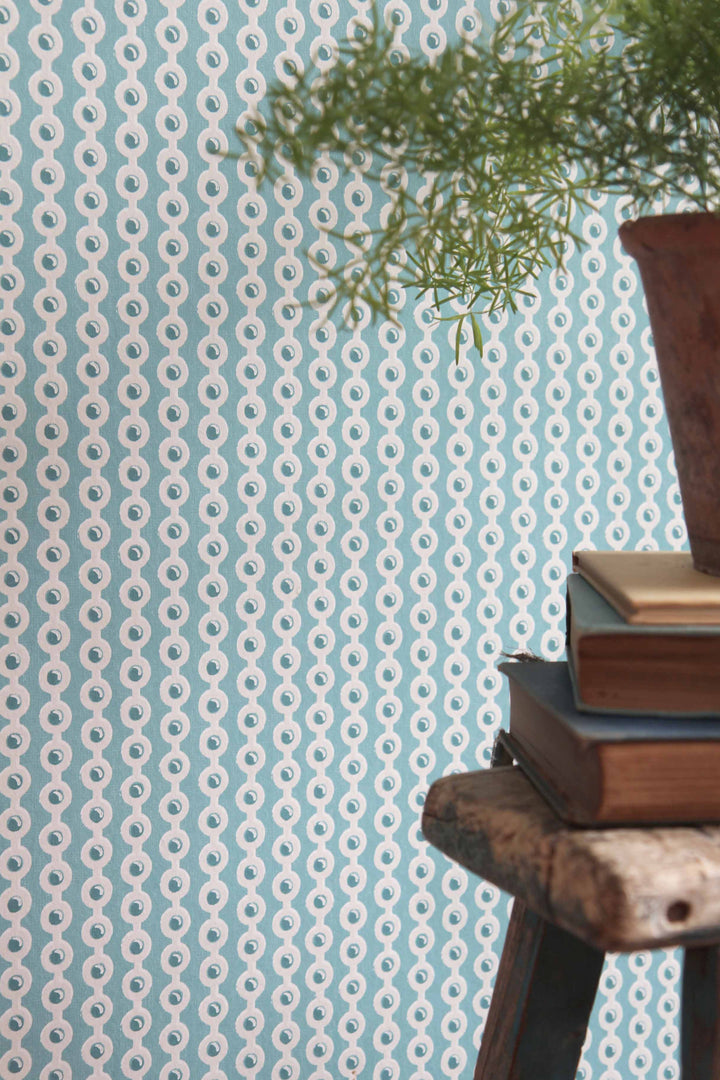 deauville spot wallpaper in celadon blue with vintage stool, pot plant and stack of vintage books