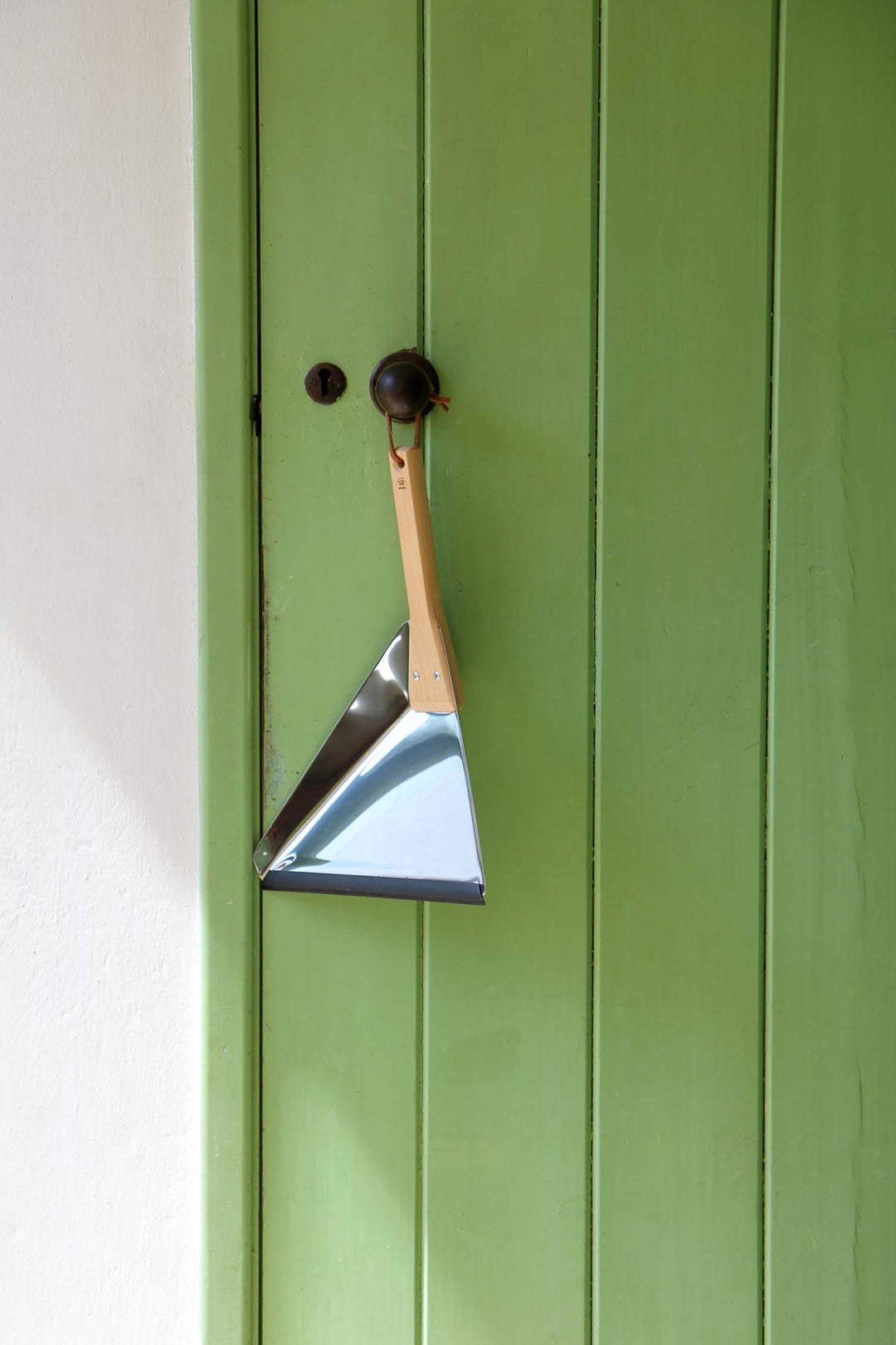 Metal dustpan hanging on a green door