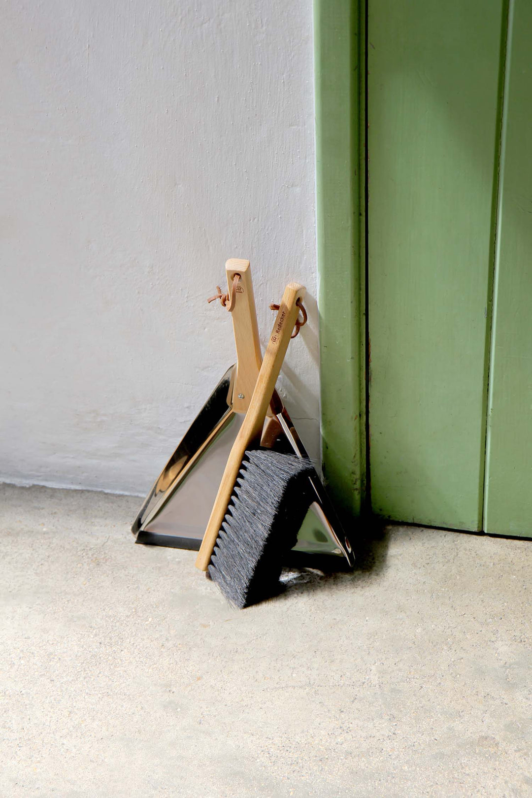 Broom and dustpan set against a green wall and gray floor.