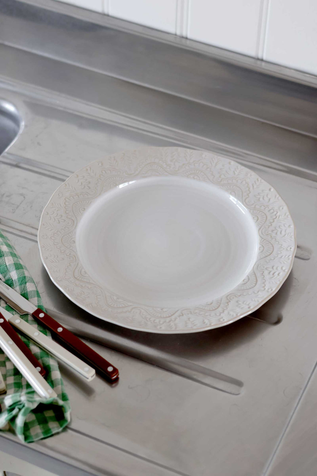 White decorative plate on a gray kitchen counter with a checkered towel and utensils.