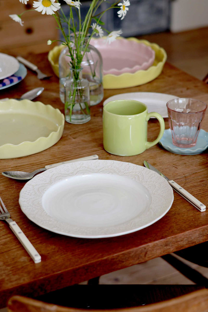 Dining table setting with plates, cups, and cutlery on a wooden surface.