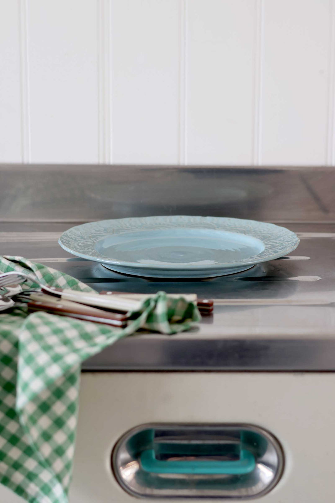 Teal plate on a stove with a green checkered towel