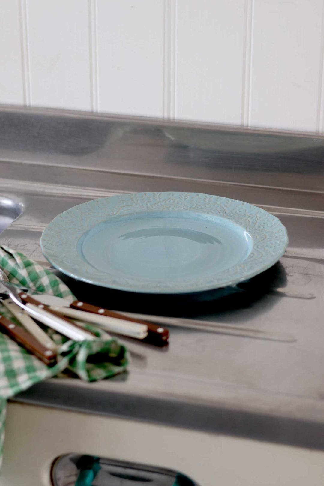 Light blue plate on a metallic surface with utensils and a checkered cloth.