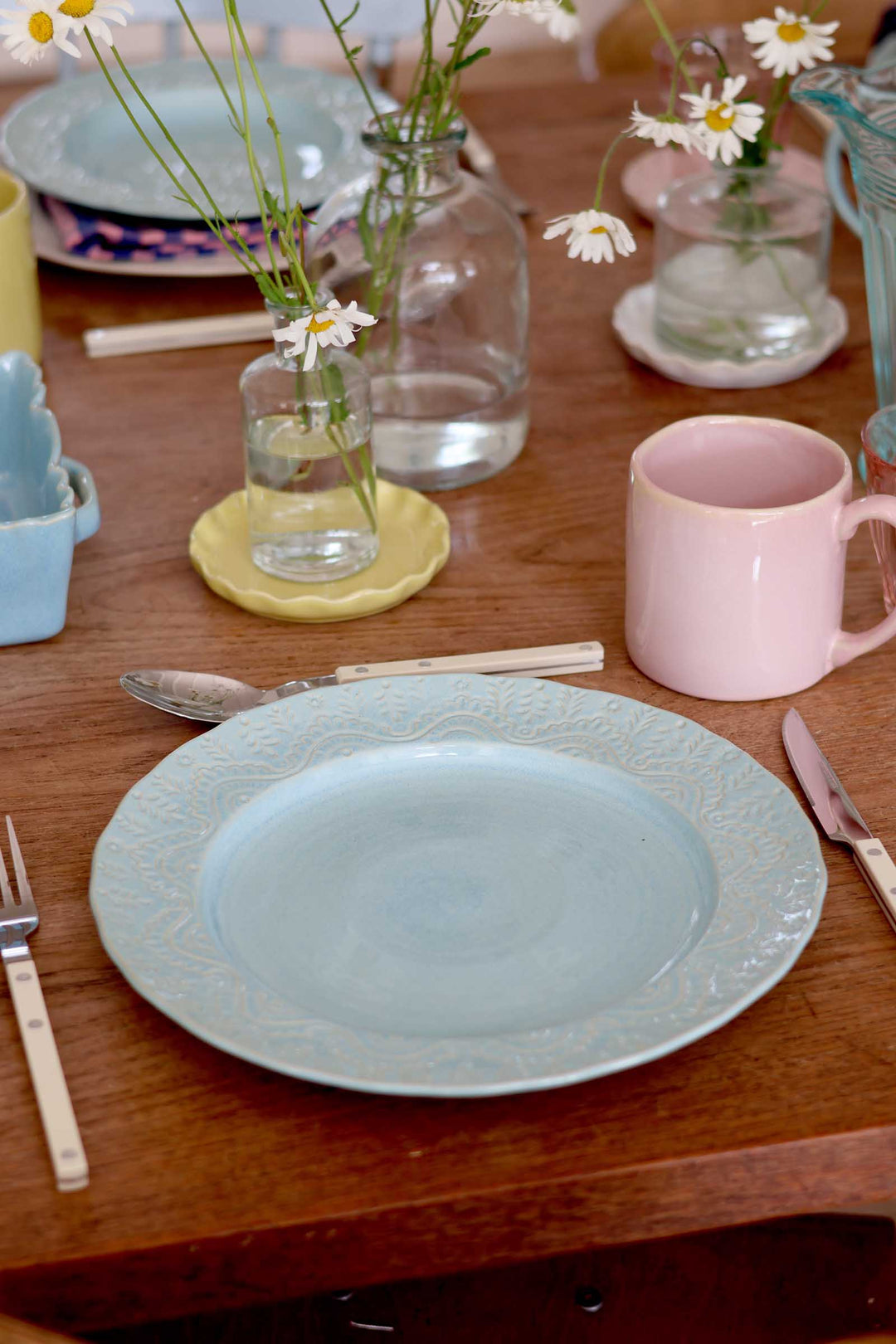 Dining table setting with a light blue plate, pink mug, and floral decorations.