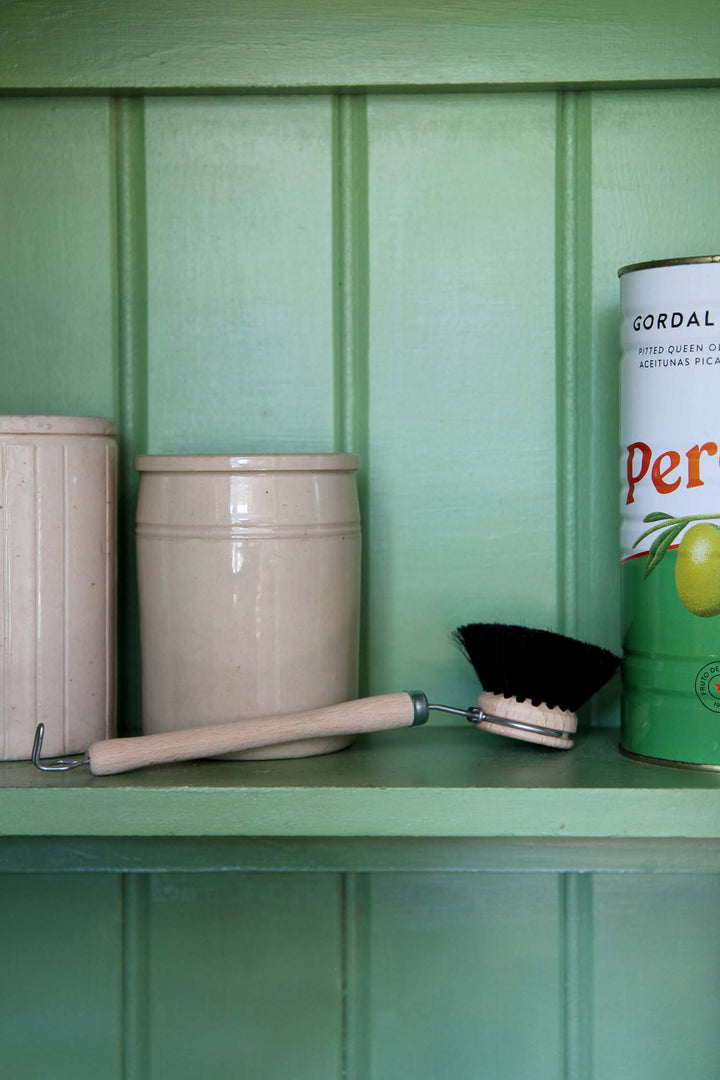Canisters and a can of Perrier on a green shelf against a green wall.