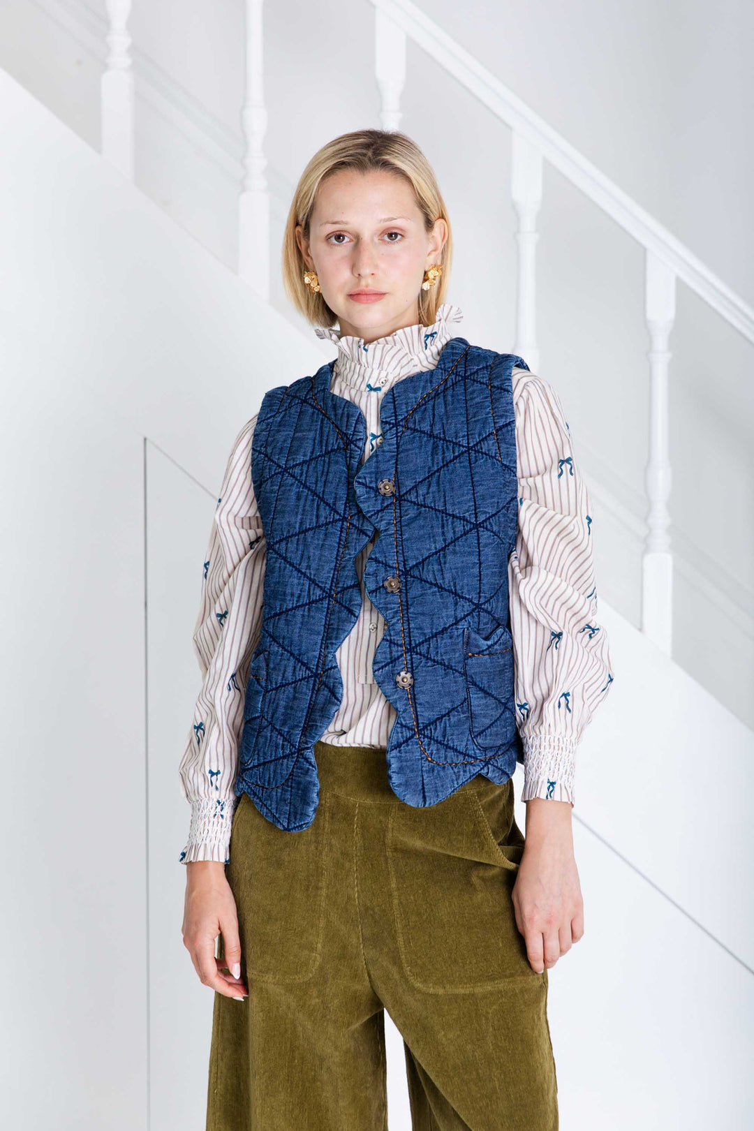 Woman wearing a blue quilted vest over a patterned shirt with a white background