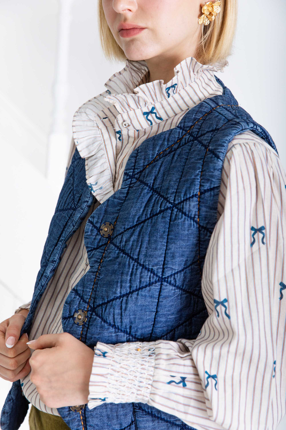 Woman wearing a blue quilted vest over a patterned shirt with a white background