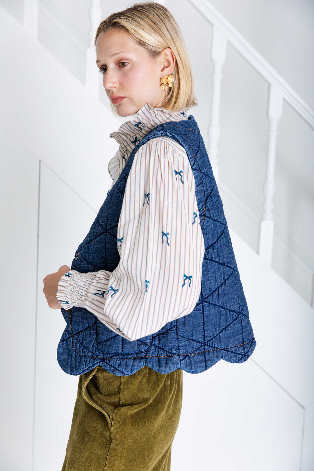 Woman wearing a blue quilted vest over a patterned shirt with a white background