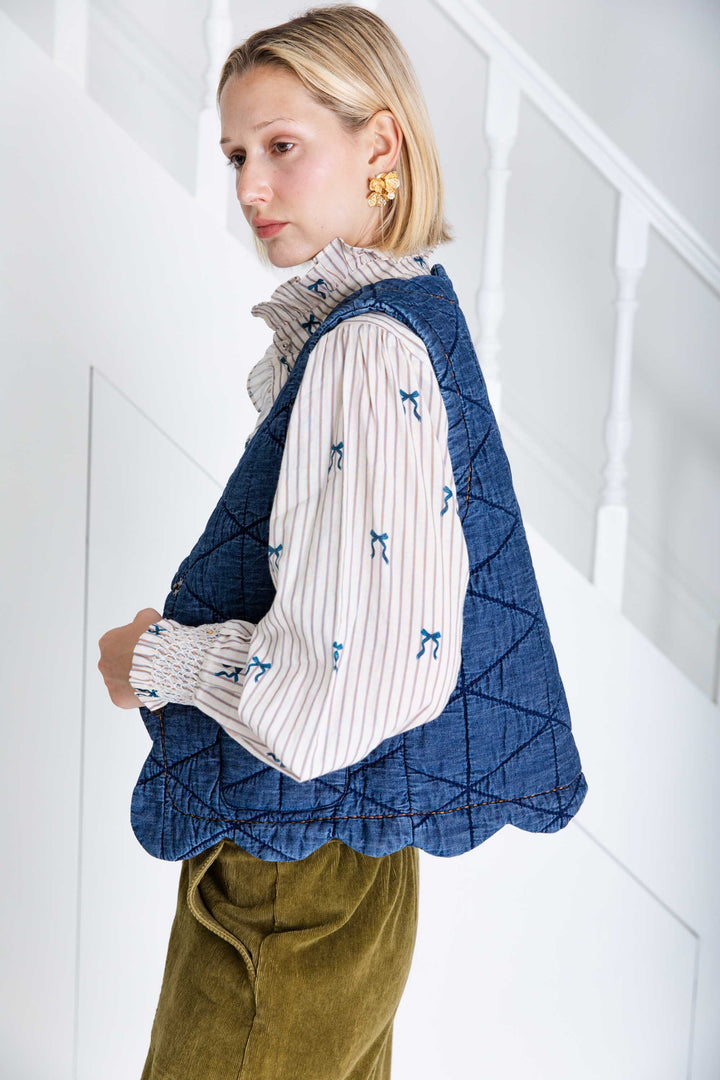 Woman wearing a blue quilted vest over a patterned shirt with a white background
