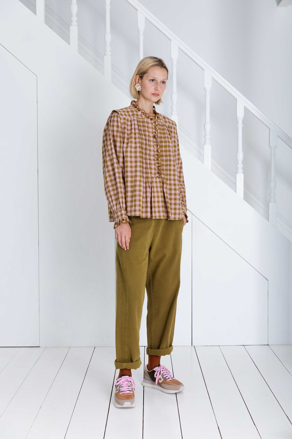 Person wearing a plaid shirt and green pants standing in a white room.