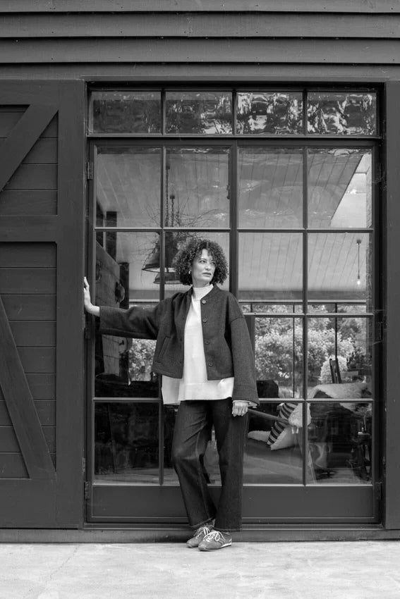 Person standing in front of a large window with a view of trees and a building.